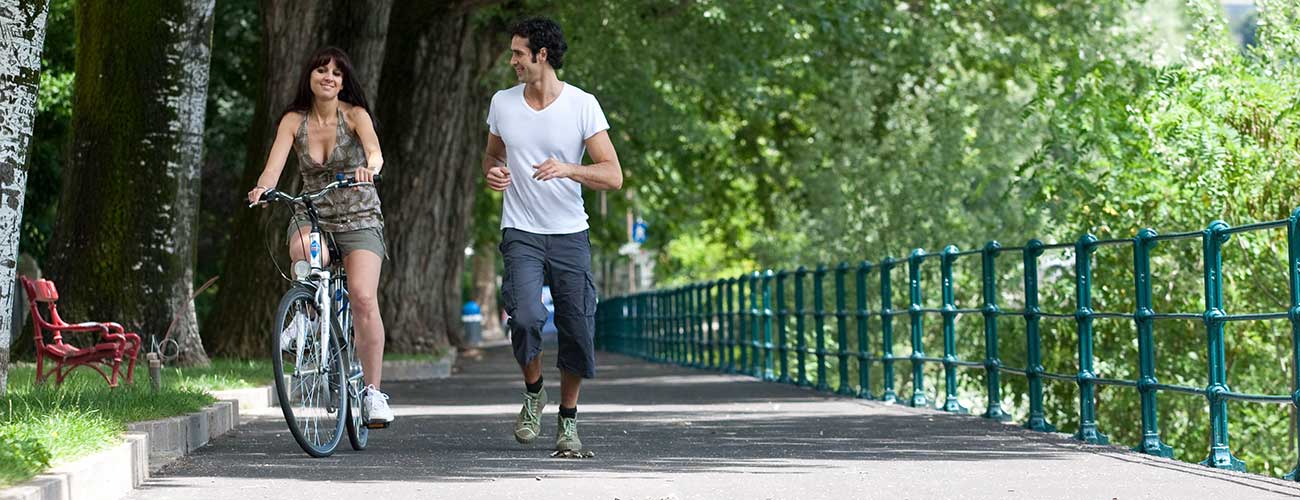 Donna in bicicletta e uomo che corre lungo il fiume Passirio a Merano